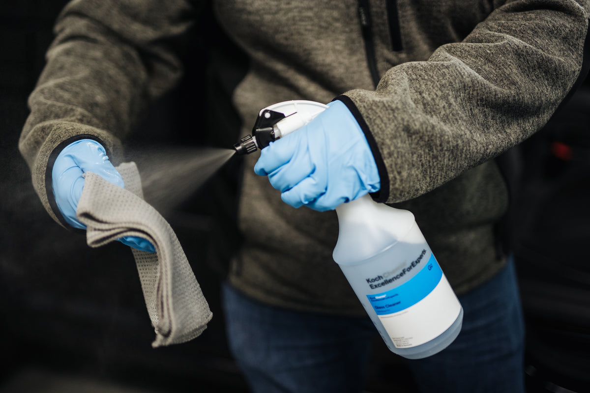 En person med blå hansker sprayer glassrengjøringsmiddel på en mikrofiberklut.