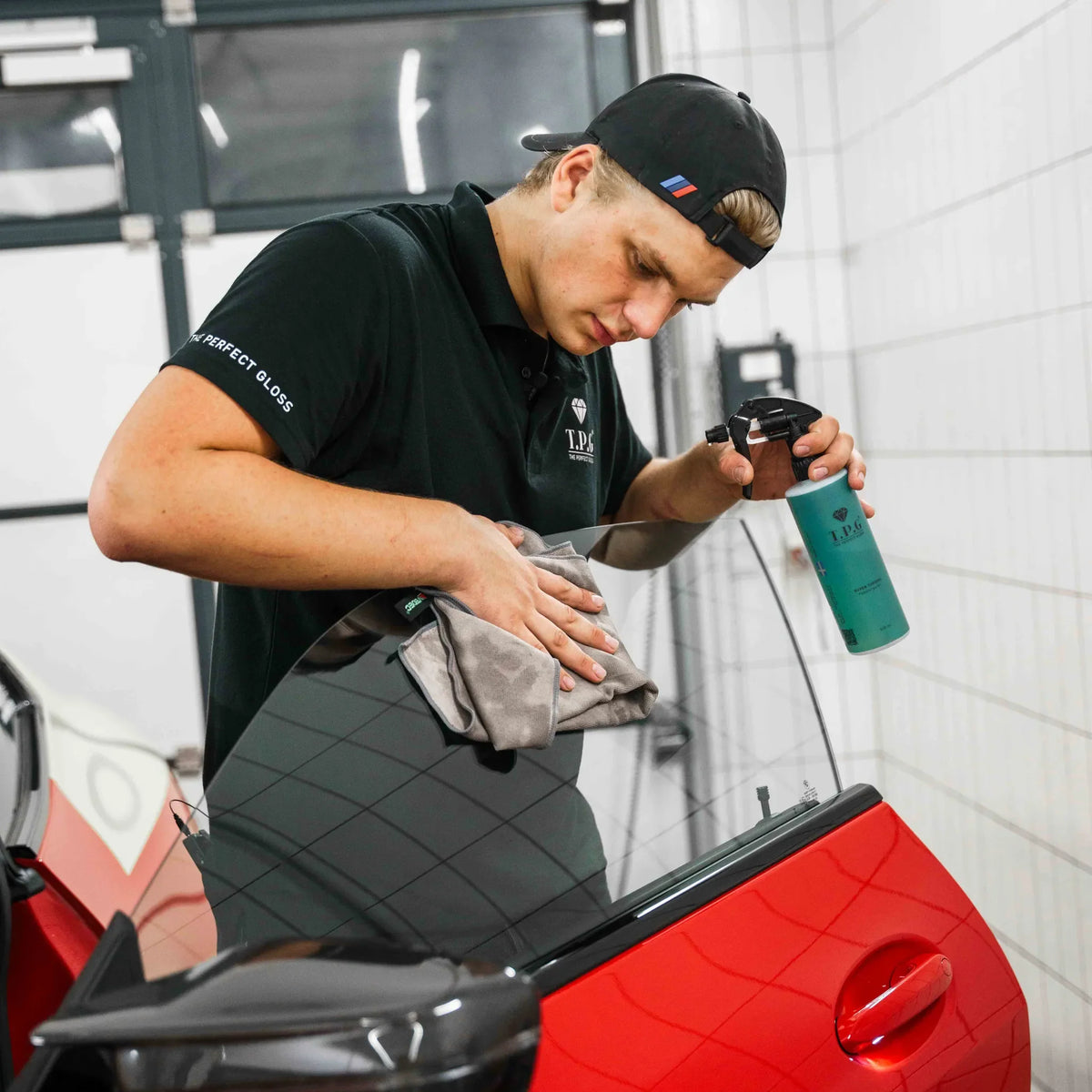 En arbeider i svart uniform sprayer rengjøringsmiddel på et bilvindu og tørker det av med en klut.