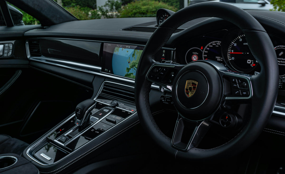 Innvendig bilde av en moderne Porsche-bil som viser rattet, midtkonsollen med girvelger, flere betjeningsknapper og et digitalt display med et GPS-kart.