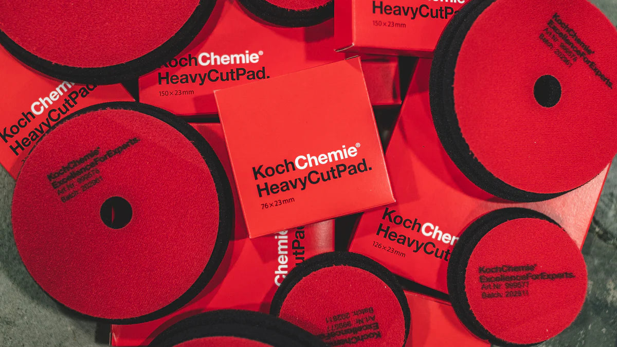 Flere røde KochChemie HeavyCutPad-poleringsputer i ulike størrelser ligger spredt utover en overflate, og merkenavnet og størrelsesangivelsene er synlige på hver enkelt pute.