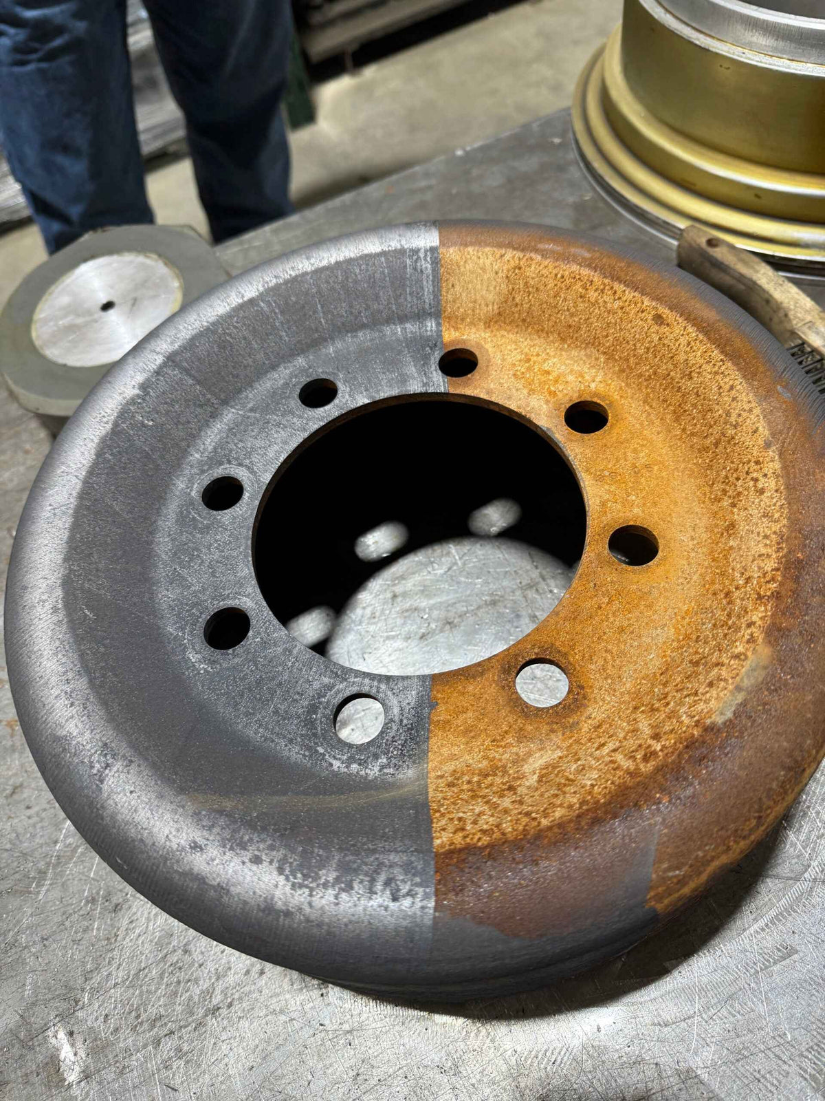 En bremseskive av metall med tydelig kontrast mellom det rustne og det rensede området, på en arbeidsbenk.