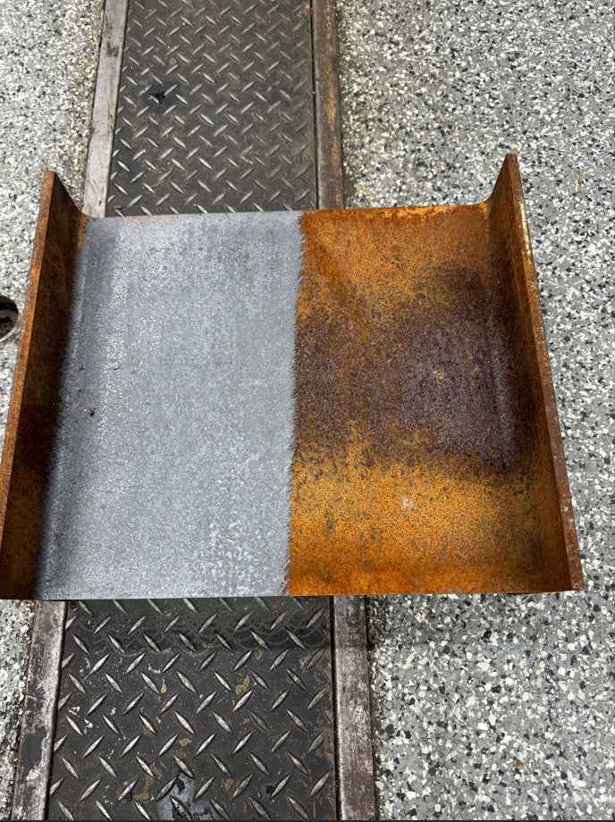 Metallplate med tydelig skille mellom den rustne og den rene siden, som ligger på betong.