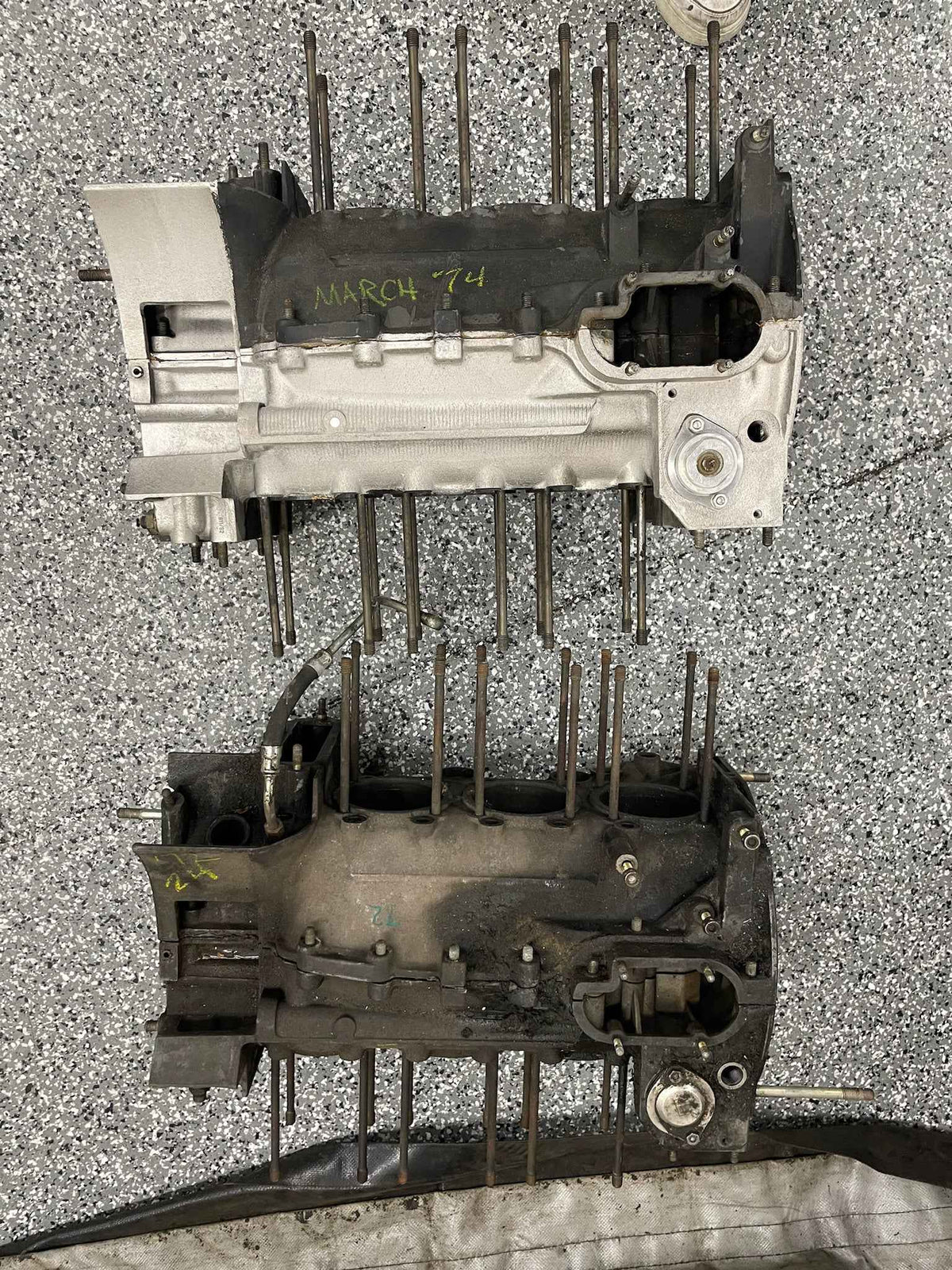 To demonterte motorblokker med studbolter, merket «March 74», står på et gulv med lysreflekser.