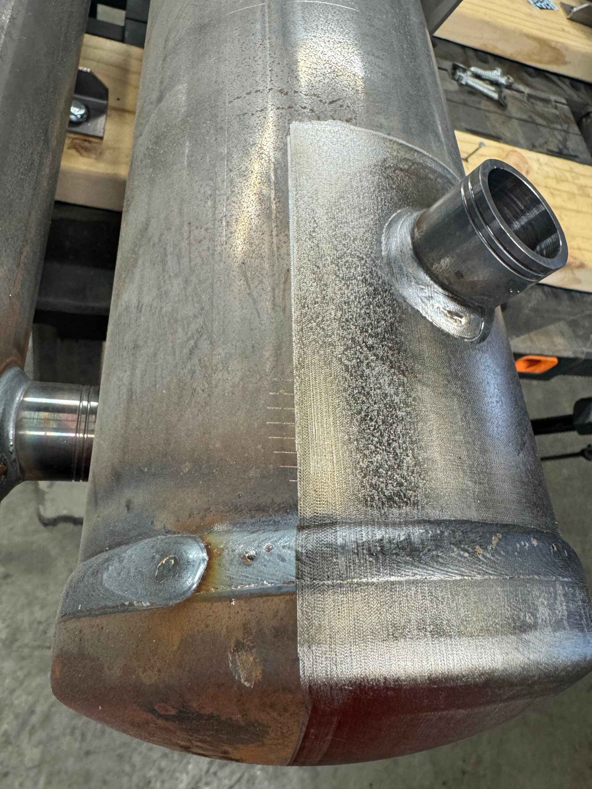 Metalltank med sveisede skjøter og et slitt område ved et utstående rør på et arbeidsbord.