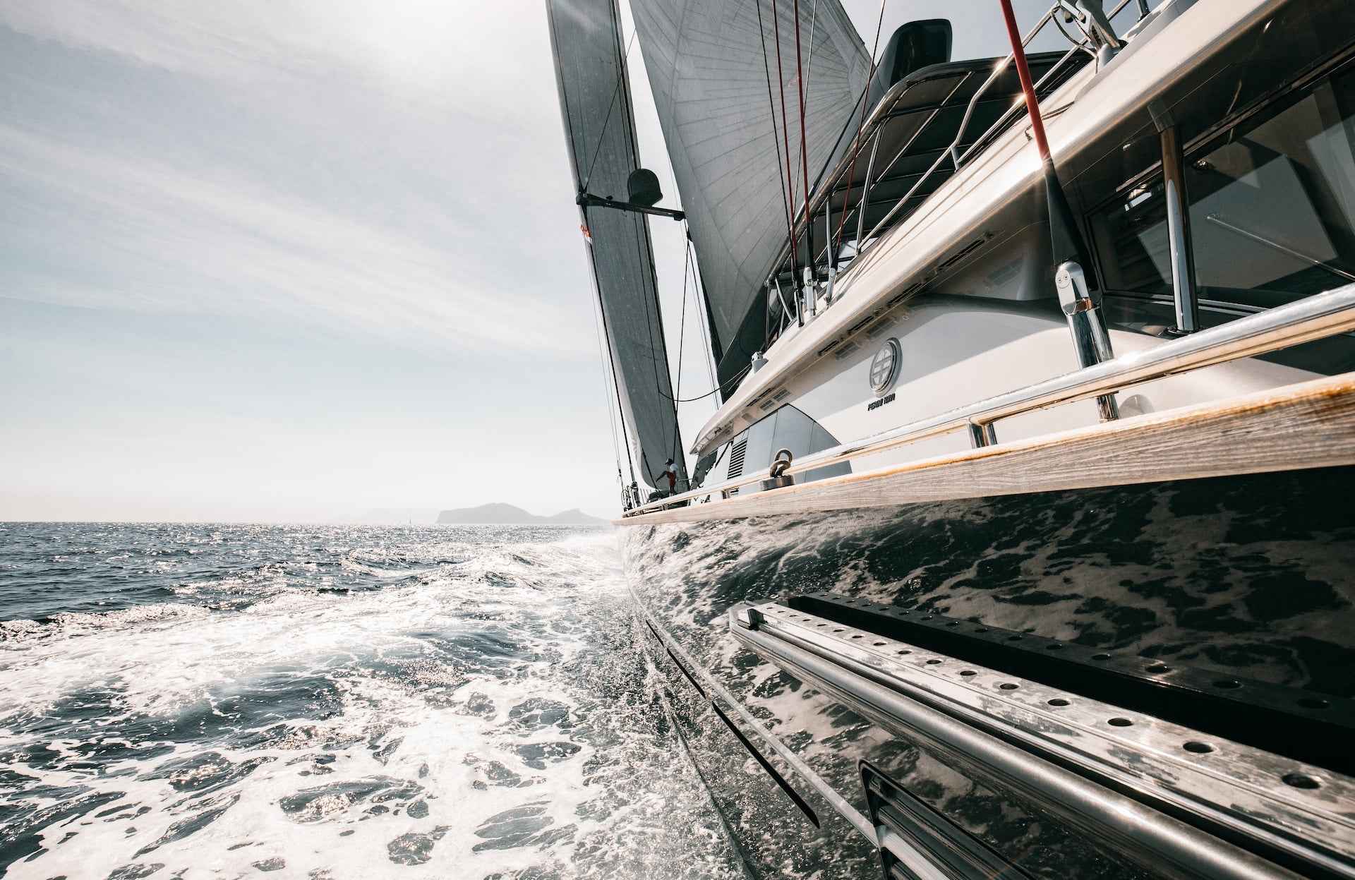En seilbåt på havet omgitt av bølger, med en øy i det fjerne.