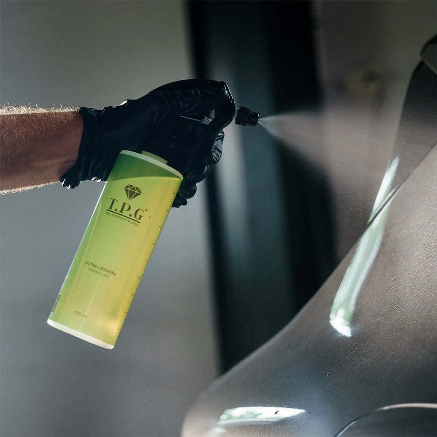 En hånd i hanske sprayer «The Perfect Gloss TPG Ultra Leggera Quickdetailer» på en grå bil.